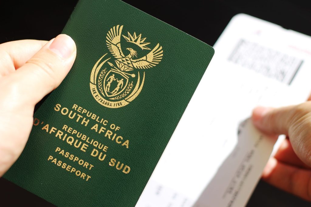 Hand holding a South African passport with a plane ticket