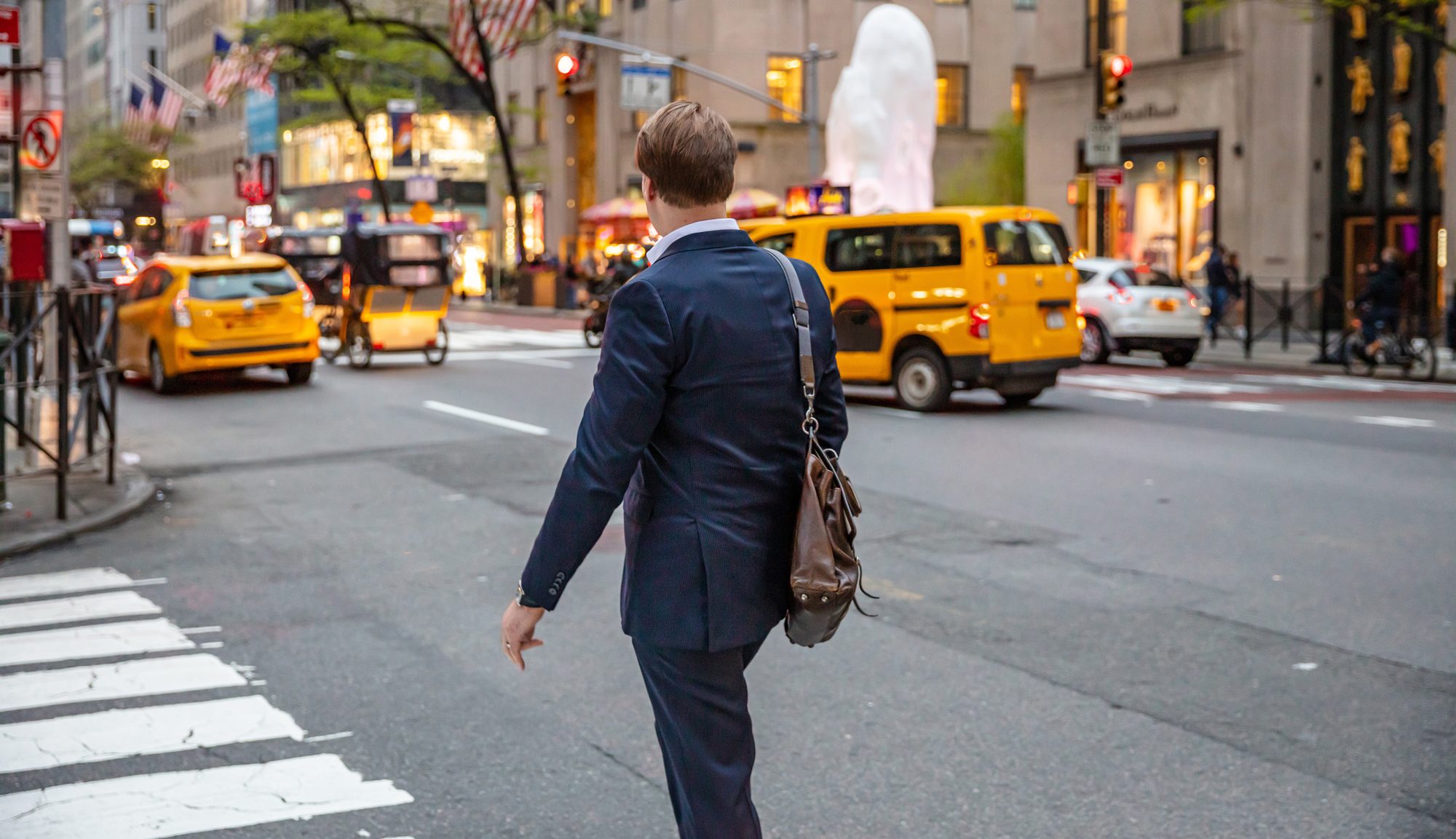 Professional in a navy suit crossing a Manhattan street with yellow cabs behind