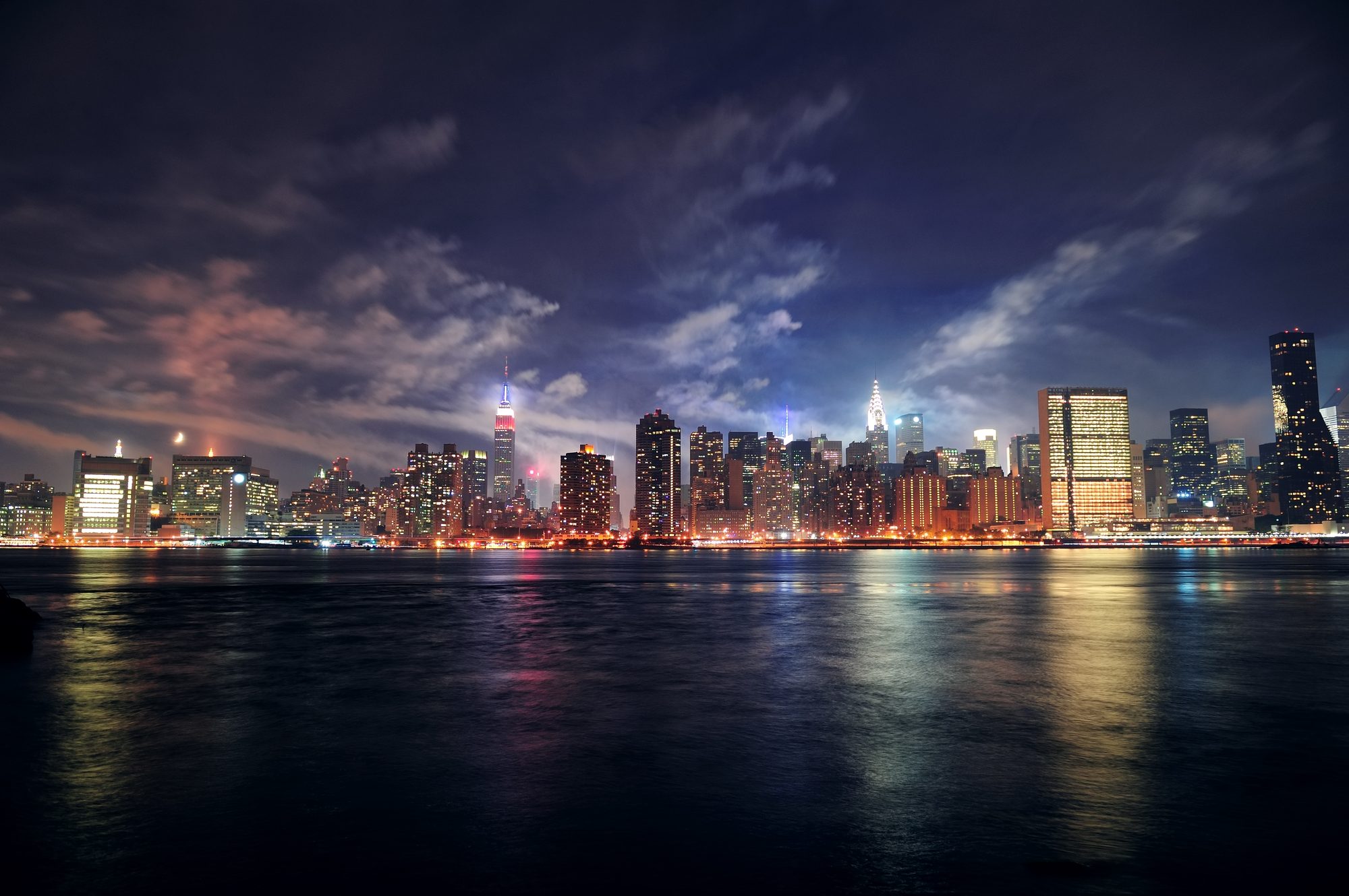 Manhattan skyline at dusk seen across the East River, lights coming on in the towers