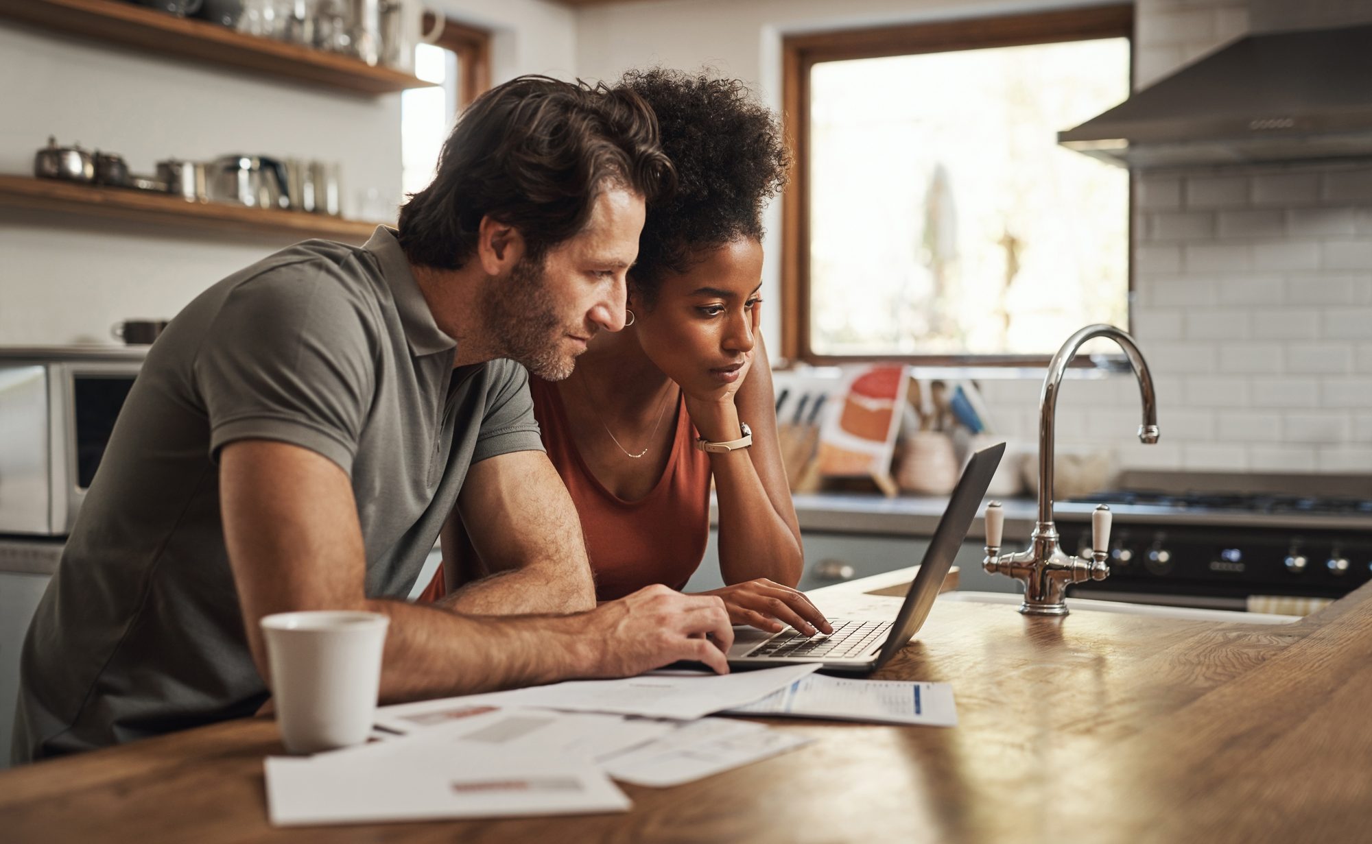 Couple at a kitchen counter planning with a laptop and papers in warm light