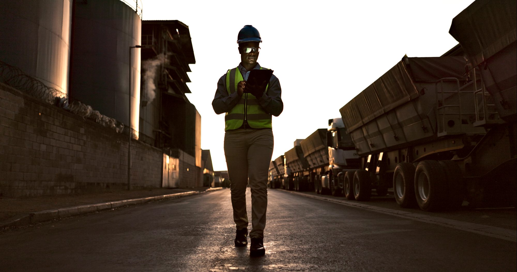 Site inspector in high visibility gear walking a haul road at dawn with a tablet