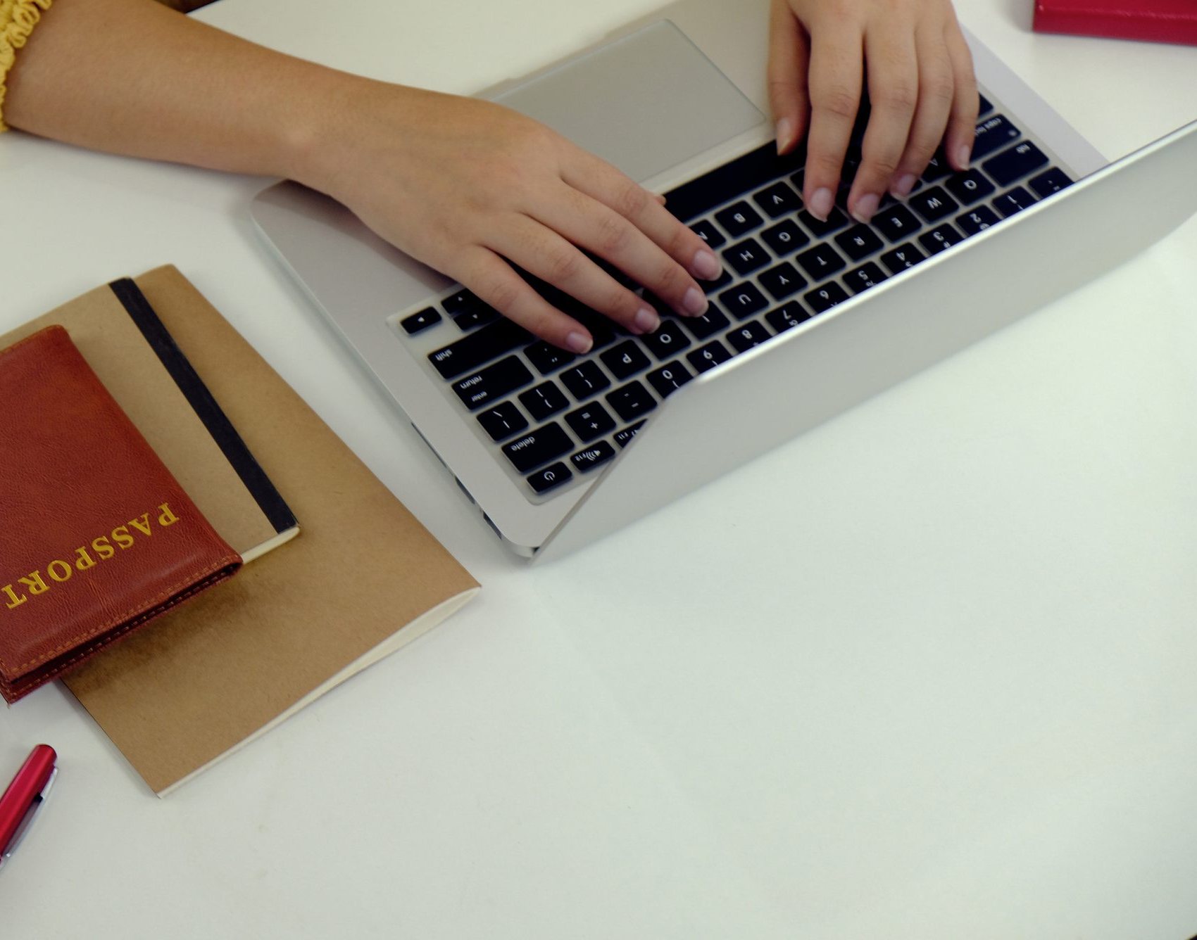 Hands typing on a laptop beside a passport on a desk