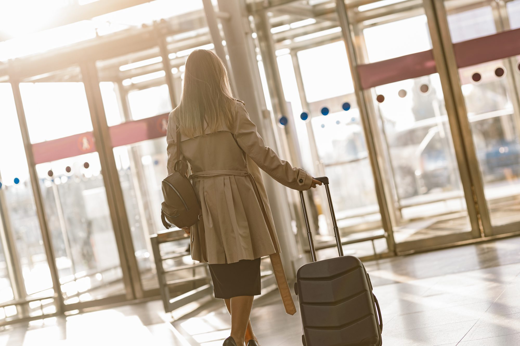 A traveller pulling a suitcase towards the doors of an airport terminal
