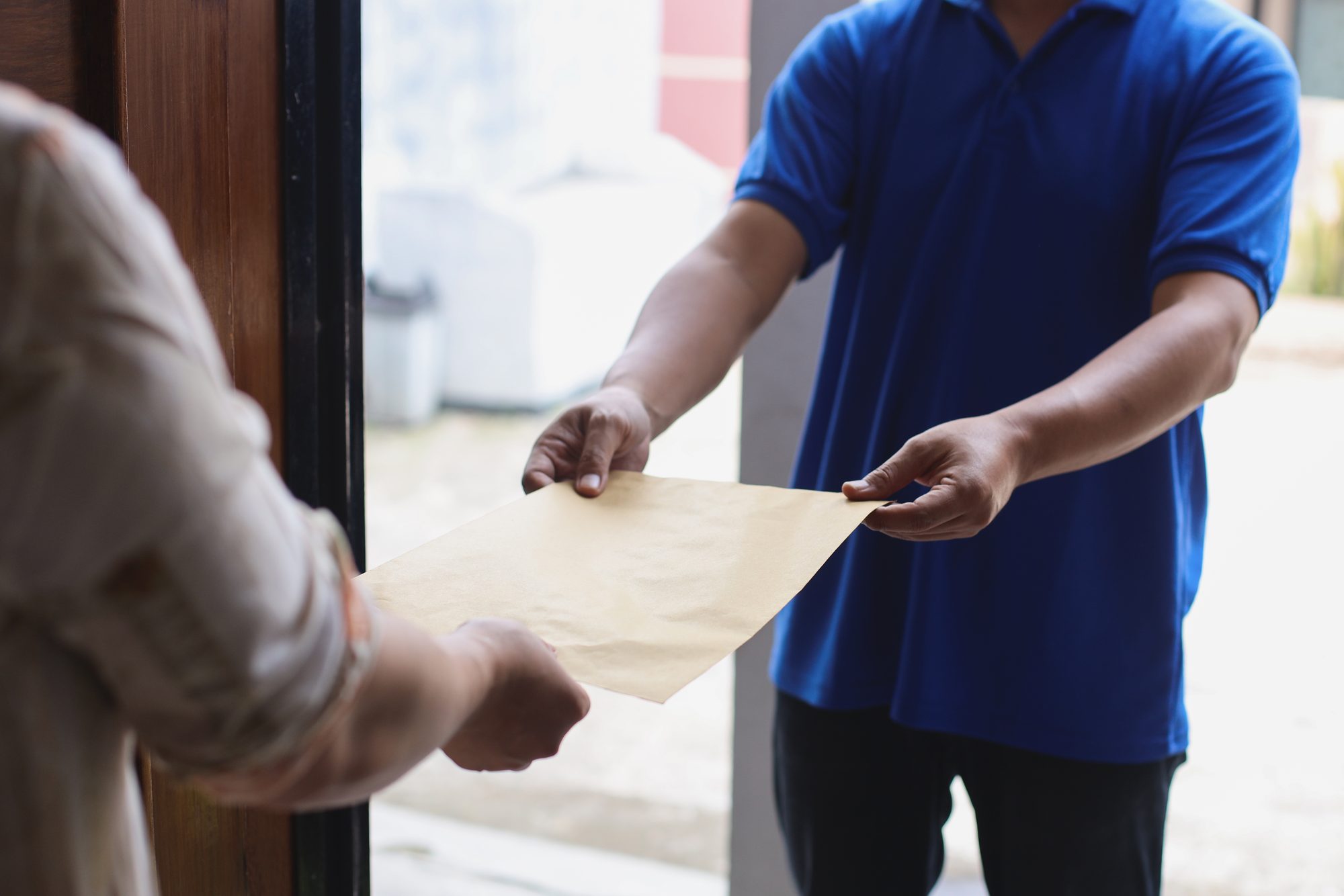 A courier handing a brown envelope to someone at a front door