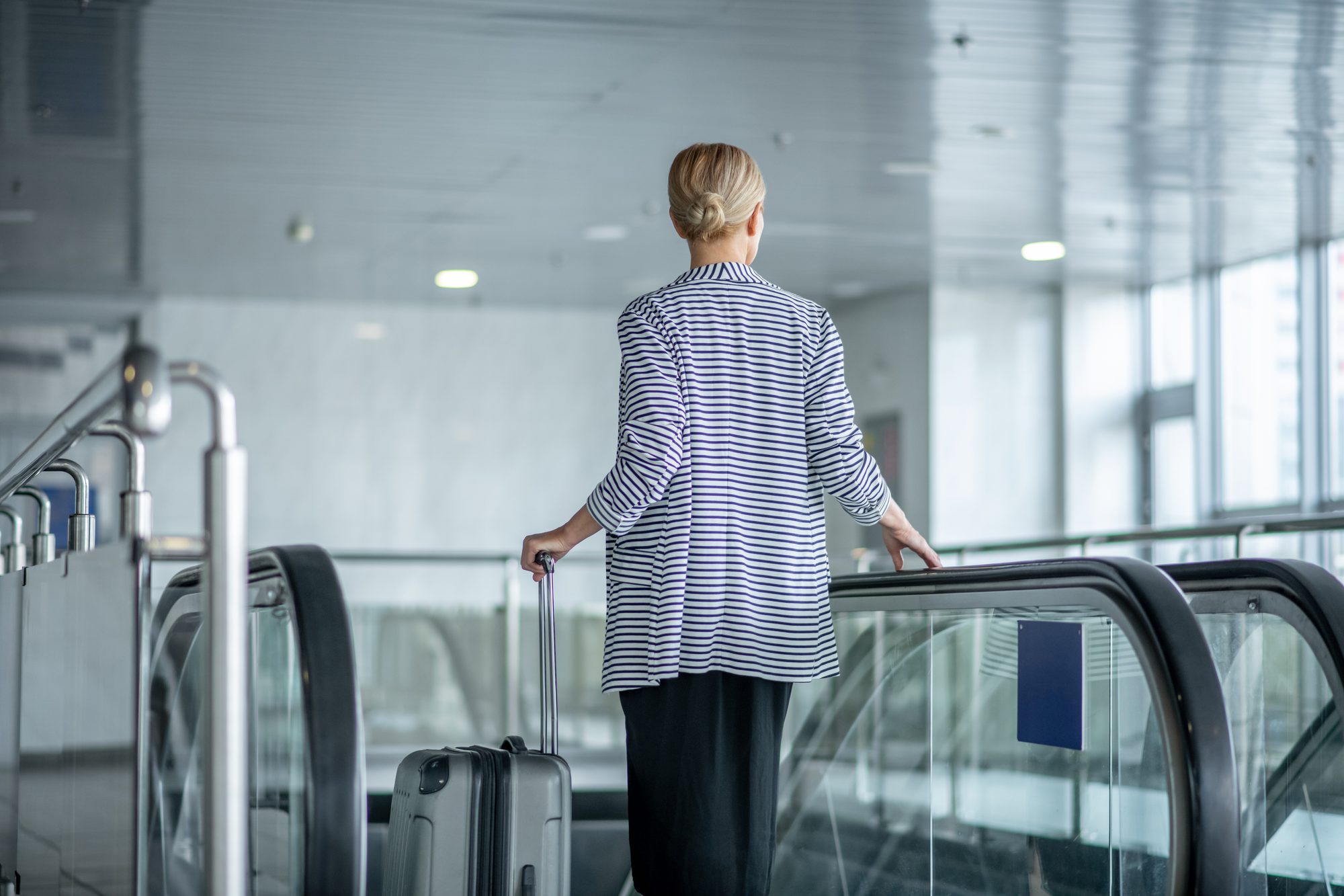 A traveller with a carry-on suitcase stepping onto an escalator in an airport terminal