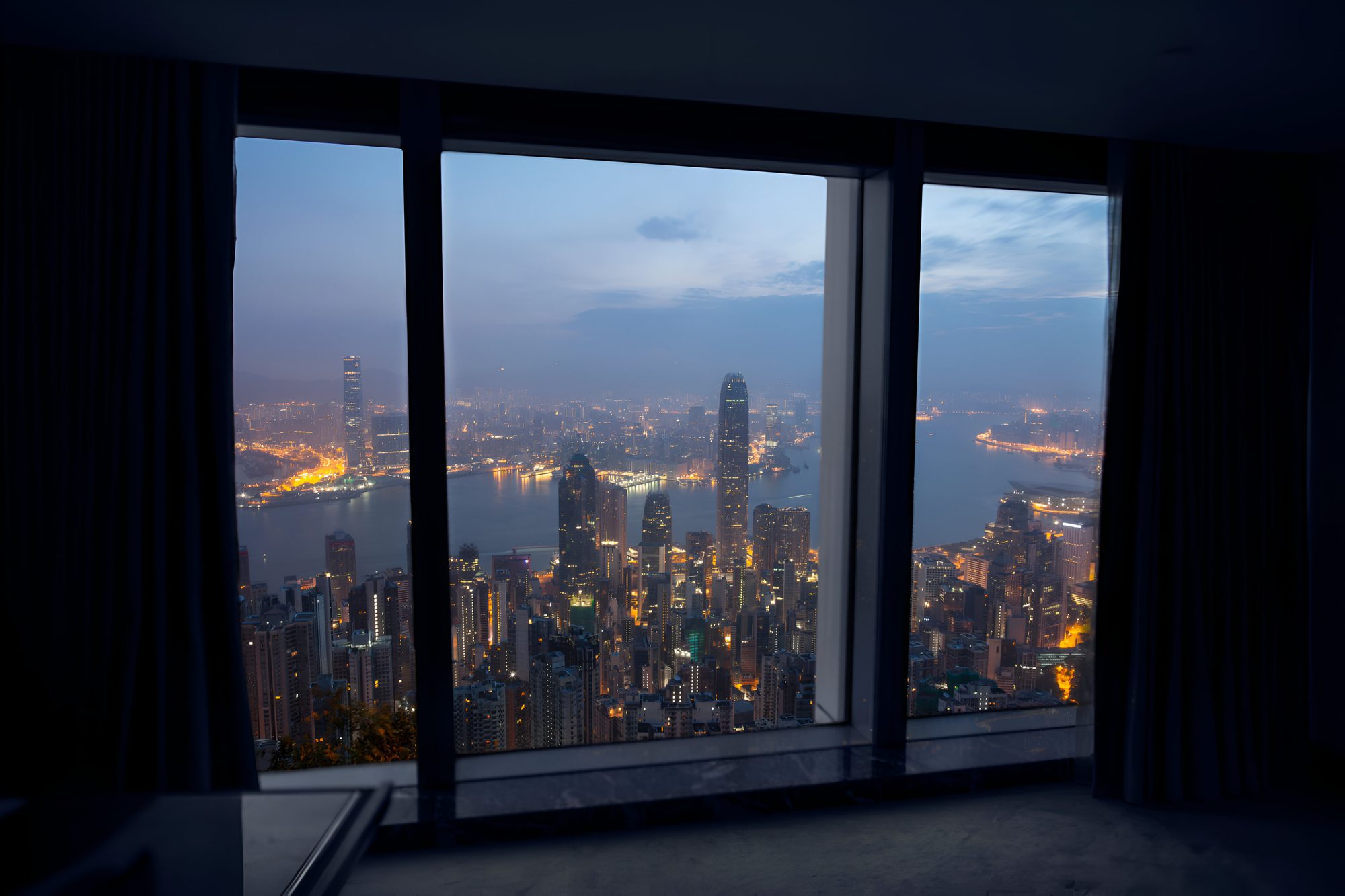 The Hong Kong skyline and harbour at dusk, seen through a high-rise window