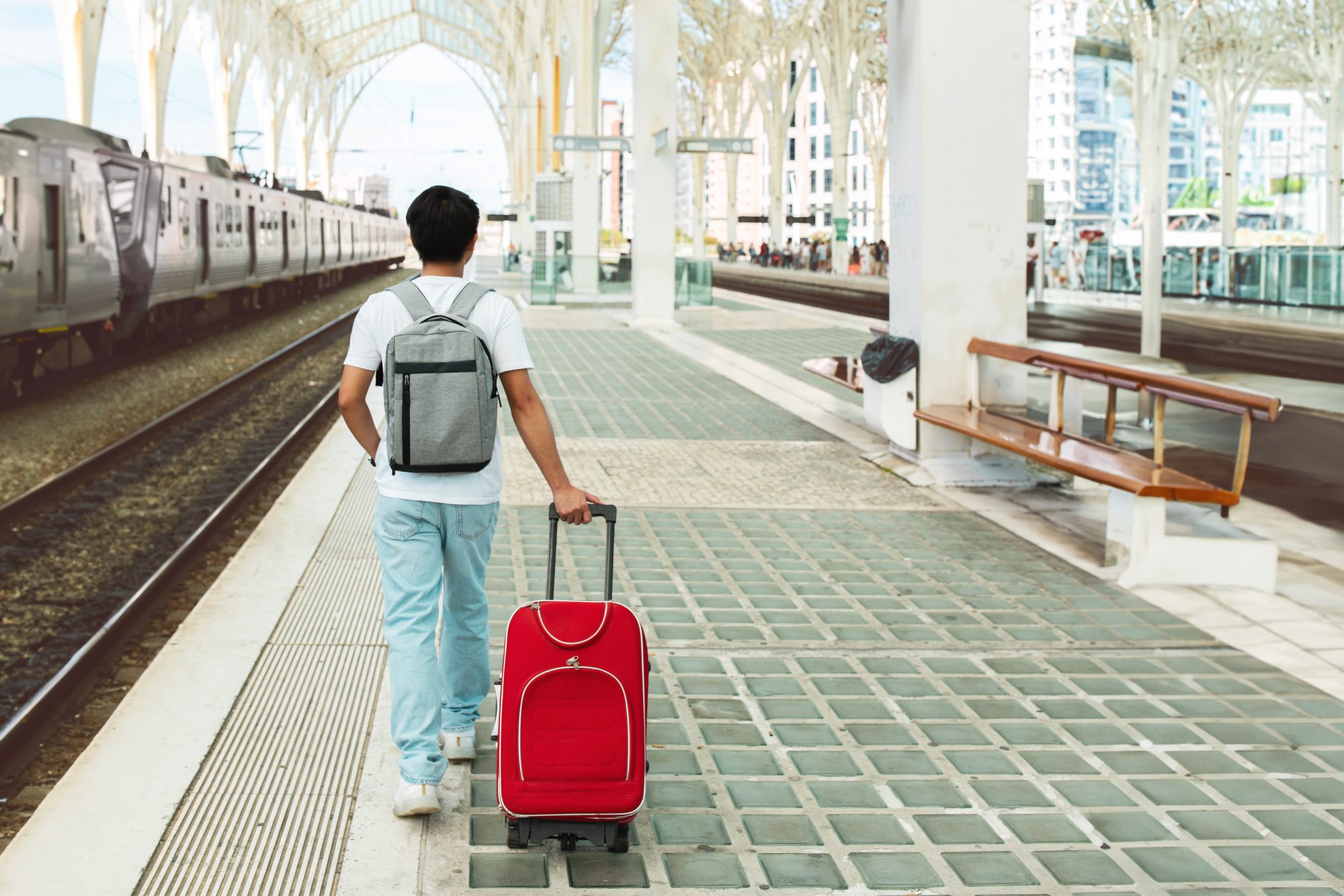 A traveller pulling a red suitcase along a railway station platform