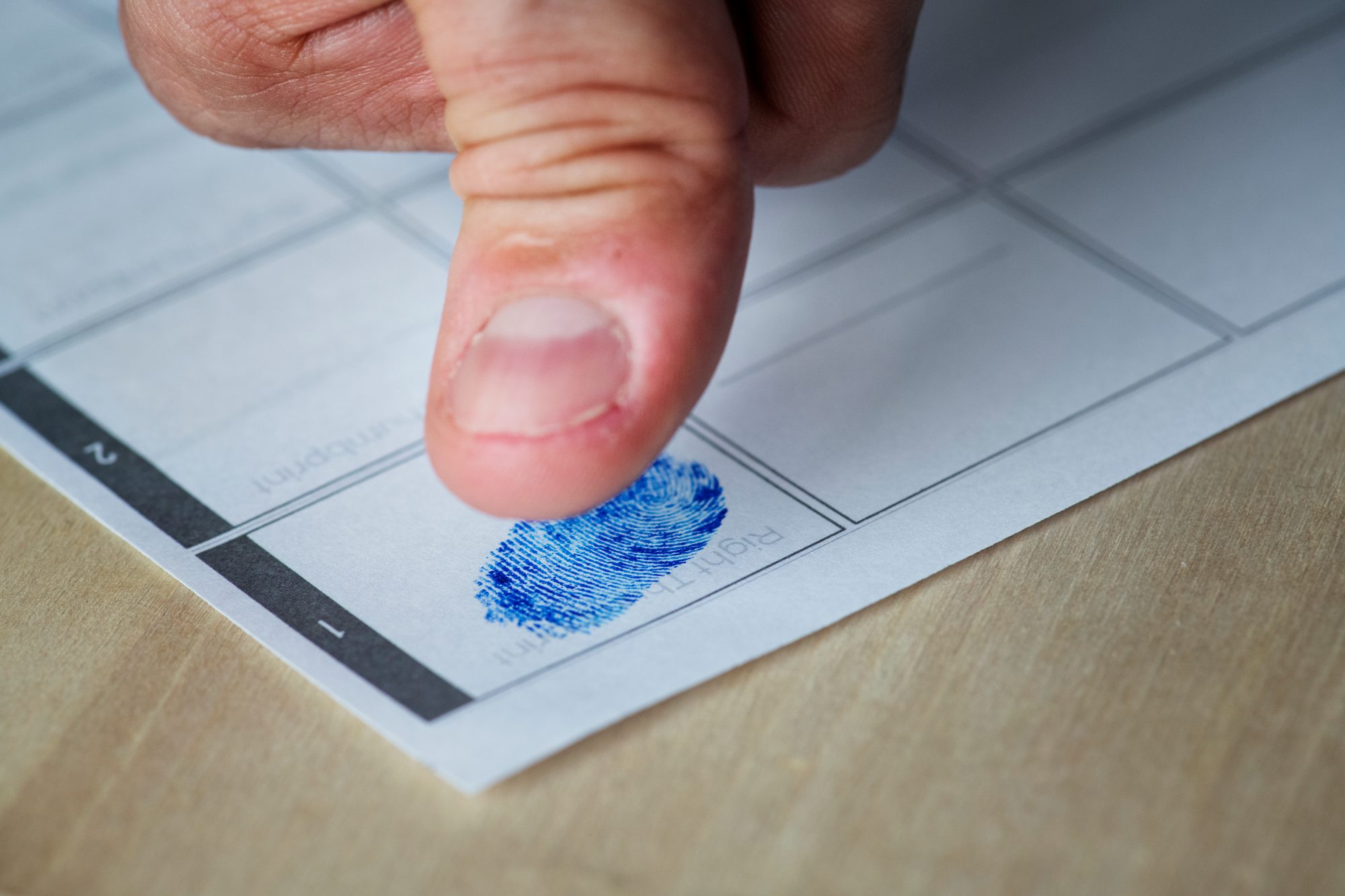 A thumb leaving an ink fingerprint on a paper fingerprint form